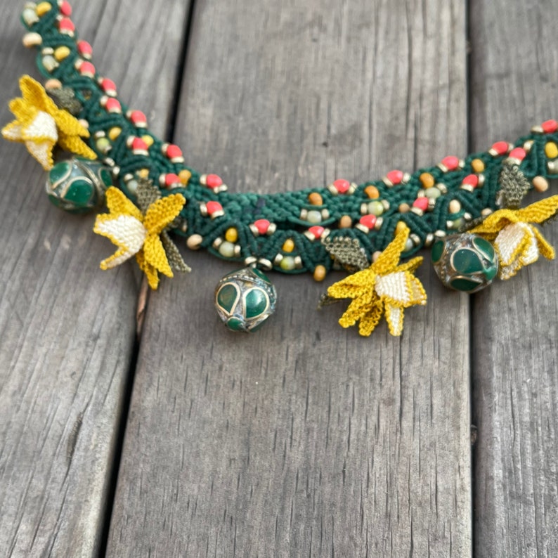 May include: A green, red, and yellow macrame necklace with small green and gold beads and yellow flower accents.
