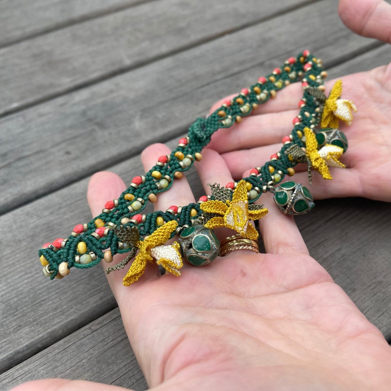 May include: A green and red beaded bracelet with yellow crocheted flowers and green and silver beads.