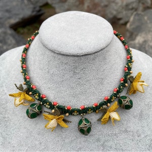 May include: A green and red beaded necklace with yellow crocheted flowers and green glass beads hanging from it.