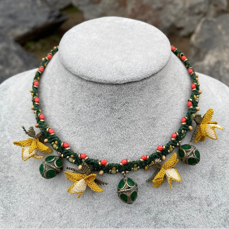 May include: A green and red beaded necklace with yellow crocheted flowers and green glass beads hanging from it.