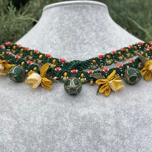 May include: A green and red beaded necklace with yellow flower accents and green and silver pendant charms.
