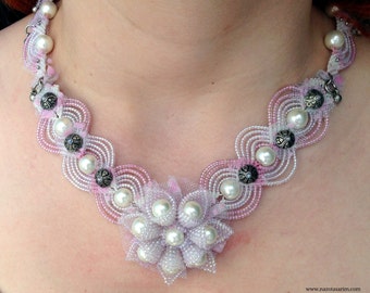 May include: A delicate pink and white beaded necklace with a large flower-shaped pendant made of pearls and lace. The necklace features a scalloped design and silver accents.