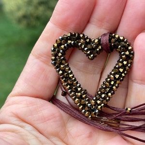 May include: A brown heart-shaped pendant made of small, faceted beads hangs from a long, burgundy cord.