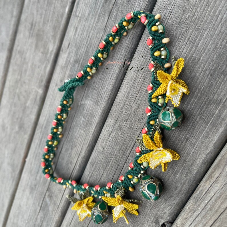 May include: A green, red, and yellow beaded necklace with crocheted flower charms and green and silver beads.