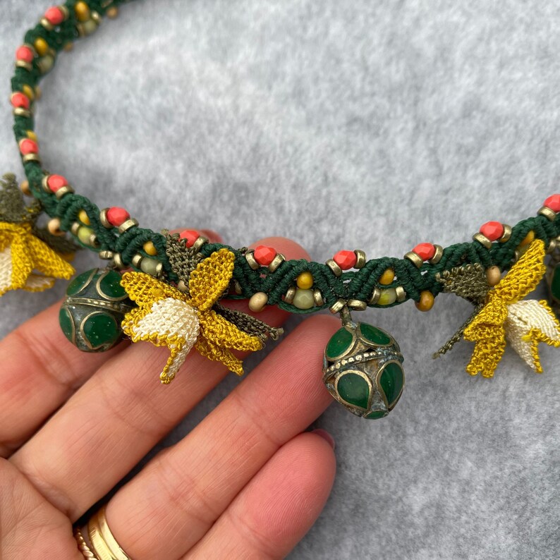 May include: A green and coral beaded necklace with yellow crocheted flowers and green metal beads.