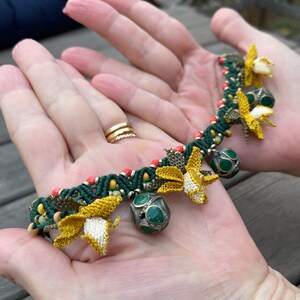 May include: A green and yellow crocheted bracelet with small bells and flower accents.