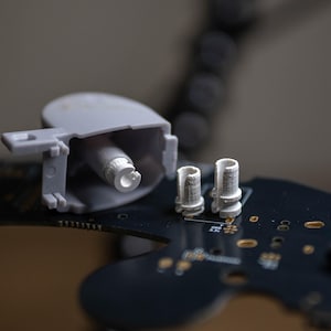 Peut inclure: Gros plan de plusieurs petits composants électroniques en plastique gris. Un composant est un boîtier rectangulaire avec une pièce cylindrique à l'intérieur. Deux composants cylindriques sont également visibles, le tout reposant sur une carte de circuit imprimé noire.