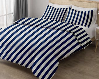 Puede incluir: Una cama con un edredón a rayas azul marino y blanco y dos fundas de almohada a juego. La ropa de cama está cuidadosamente colocada sobre la cama, que tiene un cabecero de madera clara. La habitación tiene una ventana con cortina y una mesita de noche.