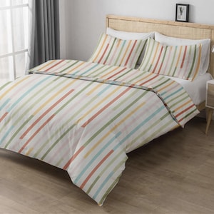 Peut inclure: Une parure de lit avec une housse de couette et deux taies d'oreiller. La literie présente un fond blanc avec des rayures diagonales colorées dans les tons de rouge, vert, jaune et bleu. Le lit a une tête de lit en bois.