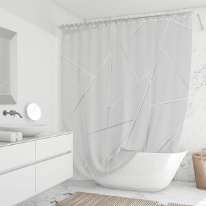 May include: A white geometric patterned shower curtain hangs in a modern bathroom. The curtain features a design of white lines and shapes. A white bathtub is in front of the curtain. The bathroom has a white vanity, sink, and mirror.
