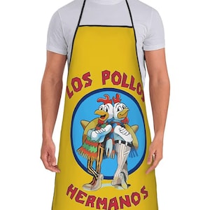 Könnte beinhalten: Gelbe Schürze mit schwarzem Rand, mit einem Cartoon-Bild von zwei Hühnern in einem blauen Kreis. Die Worte "LOS POLLOS HERMANOS" sind in fetter Schrift auf die Schürze gedruckt. Die Schürze wird von einer Person getragen.