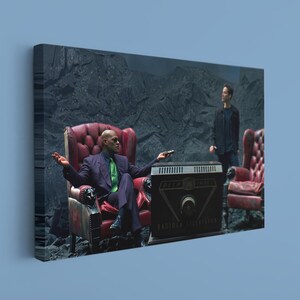 May include: A rectangular canvas print featuring a scene with two figures in a dark, rocky landscape. One figure sits in a red tufted leather armchair wearing a purple suit and green tie, while the other stands nearby. A black Radiola television sits between them.