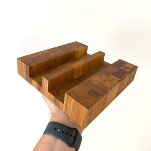 K&ouml;nnte beinhalten: Ein handgefertigter Handy-St&auml;nder aus Holz mit nat&uuml;rlicher Holzmaserung. Der St&auml;nder hat drei Schlitze zur Aufnahme eines Telefons oder Tablets. Der St&auml;nder ist aus massivem Holz und hat eine rechteckige Form, ca. 20 cm lang.