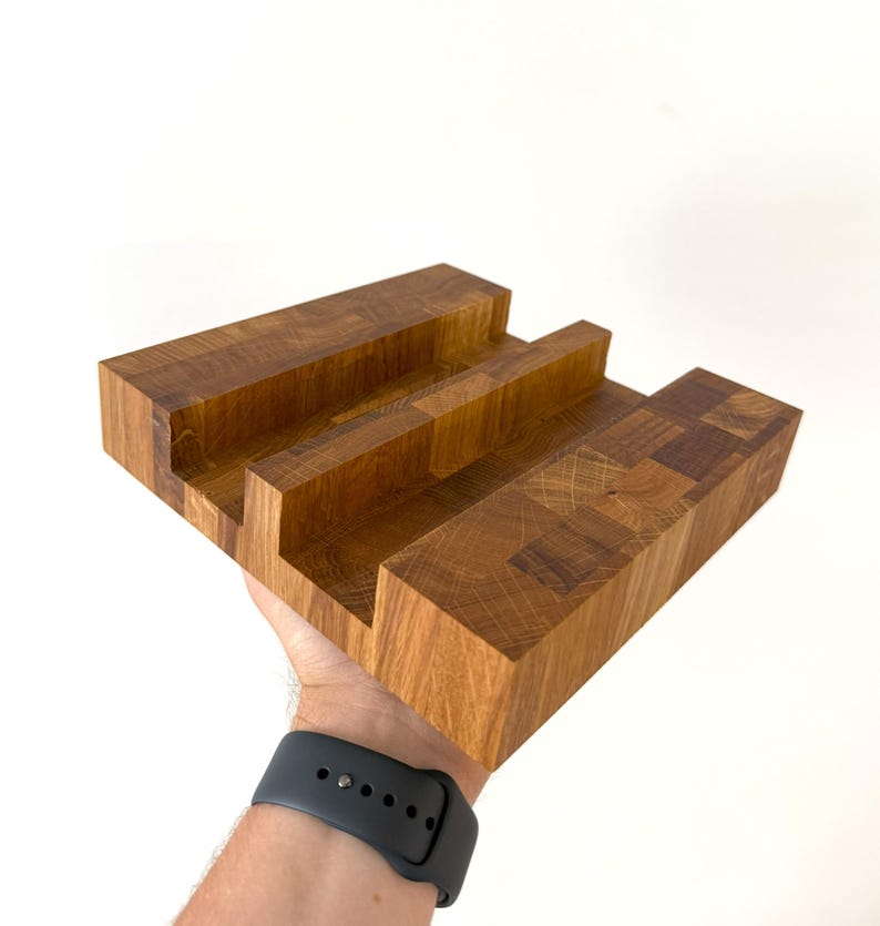 K&ouml;nnte beinhalten: Ein handgefertigter Handy-St&auml;nder aus Holz mit nat&uuml;rlicher Holzmaserung. Der St&auml;nder hat drei Schlitze zur Aufnahme eines Telefons oder Tablets. Der St&auml;nder ist aus massivem Holz und hat eine rechteckige Form, ca. 20 cm lang.