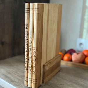 May include: A set of three wooden cutting boards with engraved titles: Fruits & Vegetables, Bread & Cheese, and Meat & Fish. The boards are displayed upright in a wooden holder, showcasing a natural wood grain finish. The boards are approximately 12 inches tall.