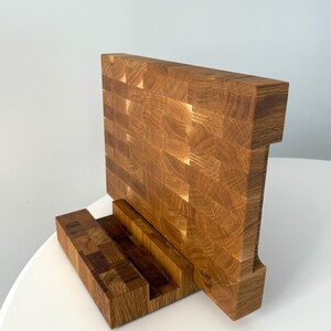 K&ouml;nnte beinhalten: Ein Holz-Schneidebrett mit einer einzigartigen Stirnholzkonstruktion. Das Brett hat eine rechteckige Hauptfl&auml;che und eine kleinere Basis, alles aus hellbraunem Holz. Das Stirnholzdesign ist sichtbar und zeigt die Textur und das Muster des Holzes.