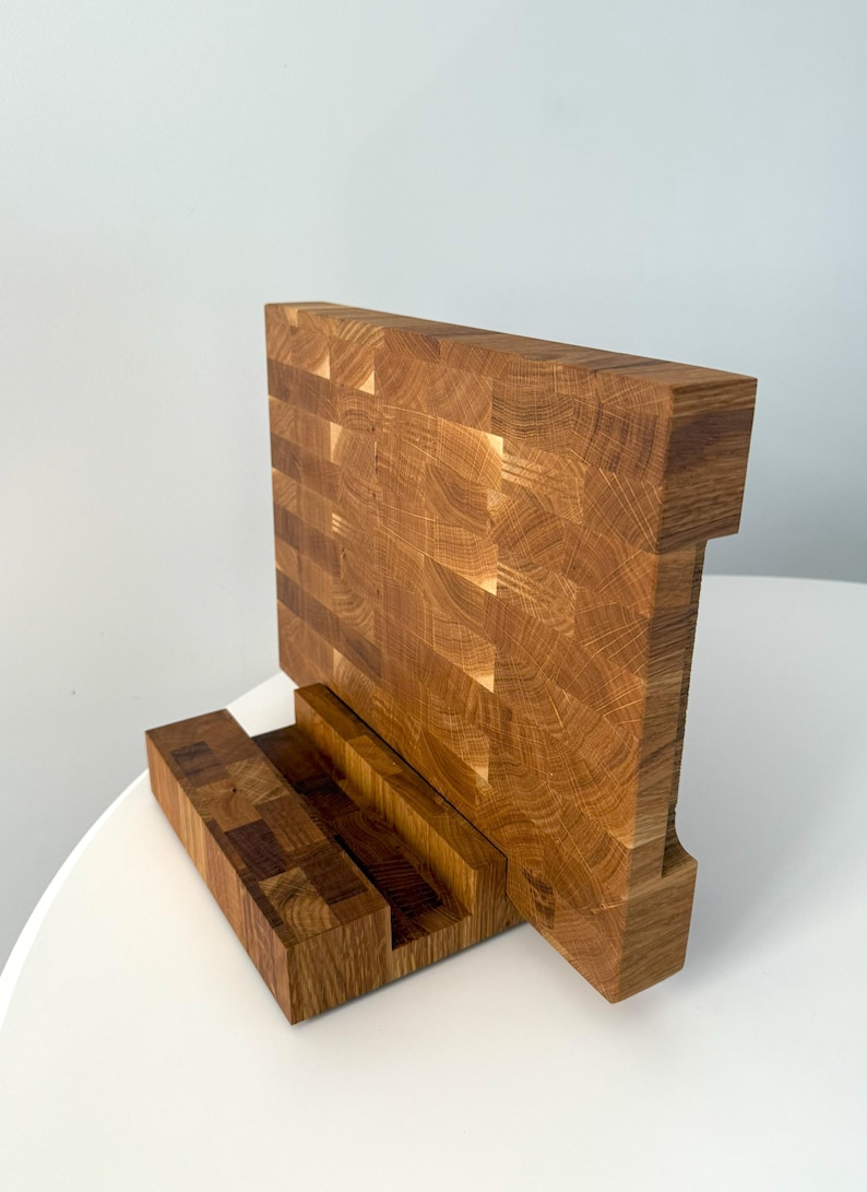 K&ouml;nnte beinhalten: Ein Holz-Schneidebrett mit einer einzigartigen Stirnholzkonstruktion. Das Brett hat eine rechteckige Hauptfl&auml;che und eine kleinere Basis, alles aus hellbraunem Holz. Das Stirnholzdesign ist sichtbar und zeigt die Textur und das Muster des Holzes.