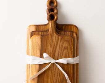 May include: A set of three wooden cutting boards with handles, tied together with a white ribbon. The boards are rectangular with rounded corners and a natural wood grain finish. The logo "eco TABULAS" is visible on the bottom board.