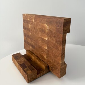 K&ouml;nnte beinhalten: Ein handgefertigtes Holzschneidebrett mit einer einzigartigen Stirnholzkonstruktion. Das Brett hat ein rechteckiges Design mit einem eingebauten St&auml;nder. Die nat&uuml;rliche Holzmaserung und die warmen T&ouml;ne erzeugen eine rustikale &Auml;sthetik. F&uuml;r die K&uuml;che.
