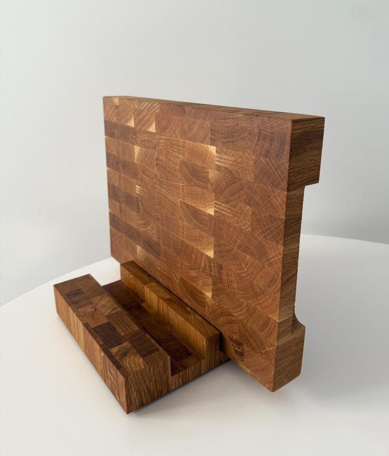 K&ouml;nnte beinhalten: Ein handgefertigtes Holzschneidebrett mit einer einzigartigen Stirnholzkonstruktion. Das Brett hat ein rechteckiges Design mit einem eingebauten St&auml;nder. Die nat&uuml;rliche Holzmaserung und die warmen T&ouml;ne erzeugen eine rustikale &Auml;sthetik. F&uuml;r die K&uuml;che.