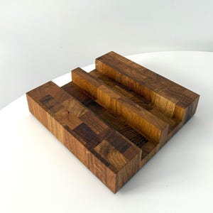 K&ouml;nnte beinhalten: Ein handgefertigter Holzst&auml;nder mit einem mehrstufigen Design. Der St&auml;nder besteht aus verschiedenen Holzst&uuml;cken, wodurch ein mosaikartiges Muster entsteht. Die nat&uuml;rlichen Holzt&ouml;ne reichen von hell- bis dunkelbraun.