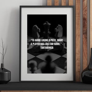 May include: Framed black and white print featuring a chess board with pieces and the quote "TO AVOID LOSING A PIECE, MANY A PLAYER HAS LOST THE GAME." by Tartakower. The print is in a black frame.