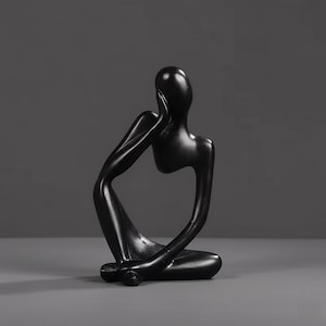 Könnte beinhalten: Schwarze abstrakte Skulptur einer sitzenden Person, ein Arm ruht auf dem Knie, die andere Hand berührt das Gesicht. Die Skulptur hat eine glatte, glänzende Oberfläche und steht vor grauem Hintergrund.