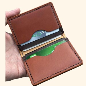 May include: Open brown leather wallet with card slots. The wallet is stitched with dark brown thread and contains several credit cards. The interior is a lighter shade of brown.