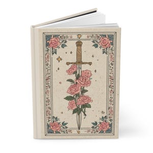 May include: A hardcover journal with a cream-colored cover featuring a decorative illustration. The illustration includes a sword piercing a bouquet of pink roses, surrounded by a floral border with stars.