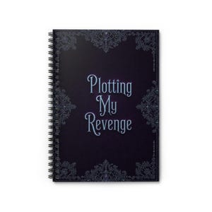 May include: A spiral-bound notebook with a dark blue cover featuring the text "Plotting My Revenge" in a stylized font. The cover is adorned with ornate, dark blue decorative elements.