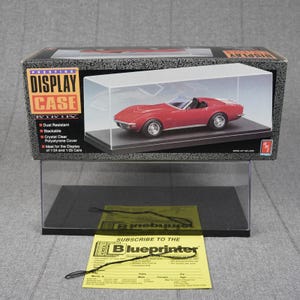 May include: A Prestige Display Case for model cars with a black base and a clear polystyrene cover. The box features text including "Prestige Display Case" and dimensions of 9 1/2 inches by 4 1/4 inches by 3 11/16 inches. A yellow subscription card is included.