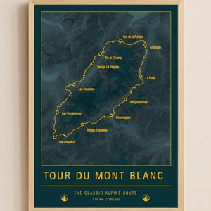 May include: A framed print depicting the Tour du Mont Blanc hiking route. The map, in yellow, is set against a dark teal backdrop, with the route's name and distance in kilometers and miles. The frame is a light wood colour.