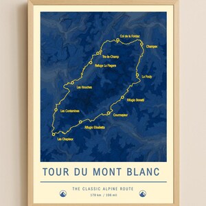 May include: A framed poster featuring a map of the Tour du Mont Blanc hiking route. The map is a dark blue with a yellow line tracing the path, highlighting locations like Les Houches and Courmayeur. The text "TOUR DU MONT BLANC" is at the bottom.
