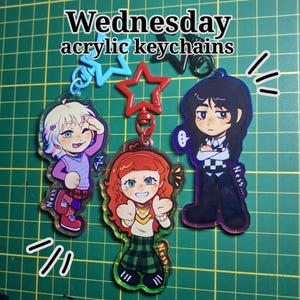 May include: Acrylic keychains featuring characters from Wednesday. The keychains have a clear background with colourful illustrations of the characters. The text "Wednesday acrylic keychains" is at the top. The keychains are attached to star-shaped and other shaped clasps.