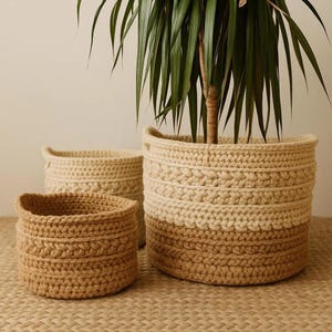 May include: Three handmade crochet baskets in varying sizes and shades of beige and brown. The largest basket holds a green plant. The baskets have a textured, woven appearance, perfect for home decor and storage.