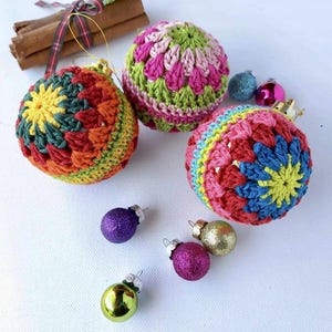 May include: A selection of colourful, handmade crochet Christmas baubles. The baubles feature a variety of bright colours, including red, yellow, green, and blue. Several small, glittery glass ball ornaments are also present.