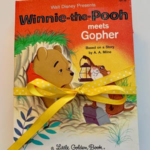 Könnte beinhalten: Ein Vintage "Winnie-the-Pooh meets Gopher" Little Golden Book. Das Cover ist orange mit Illustrationen von Winnie Puuh und Gopher. Ein gelbes Band mit weißen Punkten ist um das Buch gebunden.