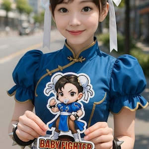 May include: A woman in a blue dress holds a sticker that says "Baby Fighter On Board" with a cartoon image of a character. The sticker has the text "Fight for the Future". The woman has white ribbons in her hair.