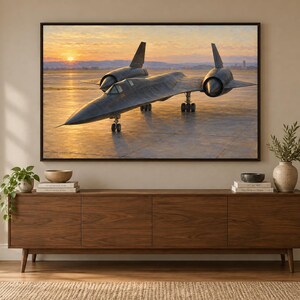 May include: A framed wall art print depicting a black SR-71 Blackbird aircraft parked on a runway during a golden sunset. The scene features the aircraft's distinct silhouette against a warm, orange-hued sky and a reflective ground surface.