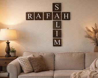 May include: A wall-mounted wooden sign spelling out the name "RAFAH SLIM" in a cross formation. The letters are white against a dark brown background. The sign is above a beige sofa with decorative pillows.