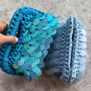 Può includere: Due borse all'uncinetto realizzate in filato spesso. La prima borsa è di un vibrante colore verde acqua decorata con paillettes circolari iridescenti e scintillanti. La seconda borsa è di una tonalità azzurro pallido con paillettes opache.