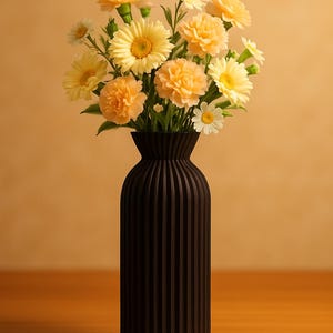 Puede incluir: Un jarrón negro con líneas verticales contiene un ramo de flores amarillas y color melocotón. Las flores incluyen margaritas, claveles y gerberas. El jarrón está sobre una superficie de madera contra un fondo beige.