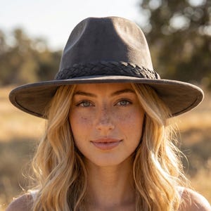 May include: A charcoal gray fedora hat featuring a wide brim and a matching braided band around the crown. The hat has a smooth, matte finish and a structured shape with a pinched top, providing a clean and classic look for various occasions.