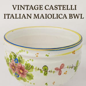 Może przedstawiać: Wazon Vintage Castelli Italian Maiolica. Biała ceramiczna misa z podstawą, ręcznie malowana we wzory kwiatowe w kolorze różowym, niebieskim i zielonym. Obręcz ma niebieskie i żółte paski. Misa ma średnicę 12,7 cm.