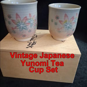 Puede incluir: Dos tazas de té Yunomi japonesas vintage con un diseño de hoja de arce en rosa, azul y verde. Las tazas están sobre una caja de madera con caracteres japoneses y el texto "Vintage Japanese Yunomi Tea Cup Set".