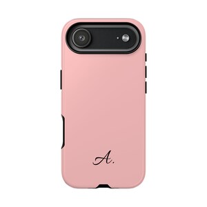 Op de afbeelding: Een lichtroze smartphonehoesje met een zwarte camerabehuizing aan de bovenkant, voorzien van een lens en flitser. Het hoesje heeft zwarte zijknoppen en een zwarte onderrand. De letter A gevolgd door een punt staat in zwarte letters gedrukt.