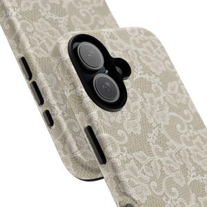 Op de afbeelding: Een beschermend telefoonhoesje met een crème-kleurig kantpatroon op een beige achtergrond. Het hoesje bevat een zwarte camerabehuizing met twee ronde lenzen en zijknoppen. Het ontwerp bedekt de achterkant en de randen van het apparaat.