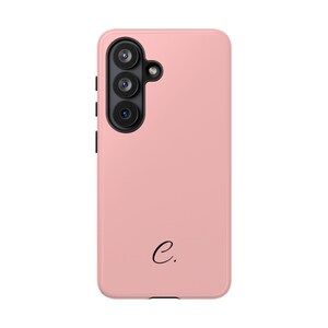 Op de afbeelding: Een effen lichtroze smartphonehoesje met een zwarte cameramodule met drie ronde lenzen en een kleine flitser. Het onderste gedeelte van het hoesje toont een kleine, zwarte, kleine letter c gevolgd door een punt in een schreeflettertype.