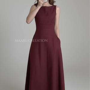 May include: A sleeveless, claret-coloured dress with a scoop neckline and a fitted bodice. The dress has a flared skirt and pockets. The text "MAARU CREATION" is printed on the dress. The dress is a midi length.