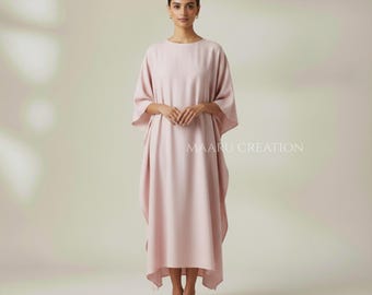May include: A light pink caftan dress with a round neckline and wide sleeves. The dress is floor-length and has a loose, flowing silhouette. The text "MAARU CREATION" is printed on the right side of the dress. The model is wearing black sandals.